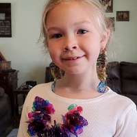 A little girl wearing earrings and a necklace she made out of recycled plastic materials. 