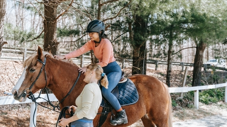 An instructor leading a horse while a student is riding on it.