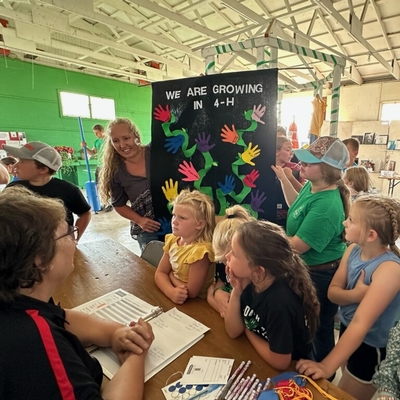 Lindsay Dalluge, 4-H volunteer, and youth members having a club banner judged at a fair.
