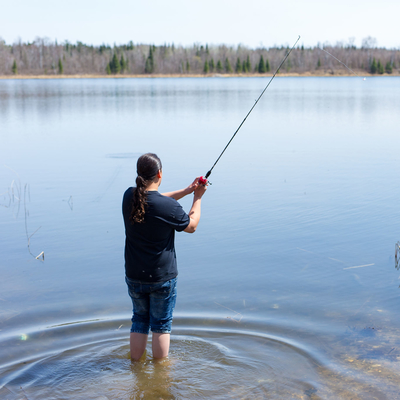 Person standing in a lake by the shore, fishing.