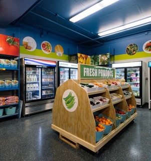 A supershelf food shelf looks like a grocery store displaying fresh produce in bins, and fresh food in cold storage. Paintings of fruits and vegetables are on the walls. 