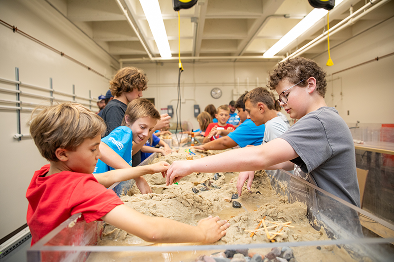 A group of youth working together to build structures in a table filled with sand.