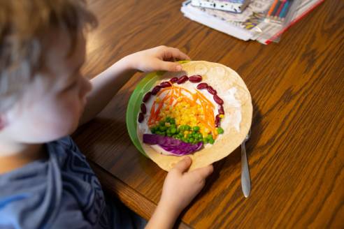 Child with a tortilla decorated with a variety of vegetables