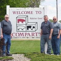 Two men to left of sign and three men to the right. Large sign reads "Welcome to Compart's" and "Mak'em Grow!"