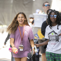 Two teen girls walking ahead of a group smiling.