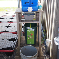 Handwashing stand built of lumber with square plastic water container sitting on top of stand