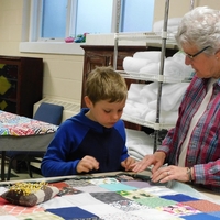 older woman and young boy work on quilt together