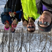 Family of six adults smiles for the camera while skiing. They are wearing a variety of winter coats and hats and there are trees behind them.
