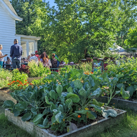 Several raised garden beds with people gathered around a picnic table in the distance