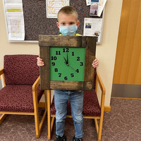 A boy holding a clock with a green face and a thick wood frame