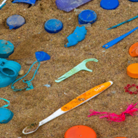 Plastic trash items arranged in rainbow order on sand.