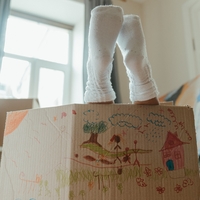 A cardboard box with two socked human feet coming out the top