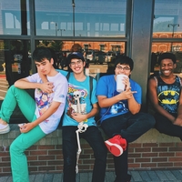 Four teen boys sitting together on a ledge of a building outside.