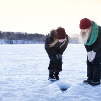 An woman and girl peer into an ice fishing hole on a frozen lake