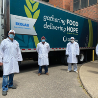 Four people in white lab coats stand outside a Second Harvest Heartland truck.