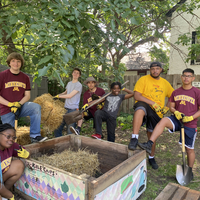 Seven Gardens for Change crew members gathered around a raised garden bed with straw