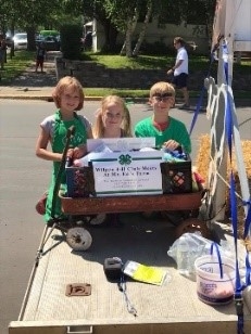 Two girls and a boy standing behind a wagon with a 4-H sign in it.