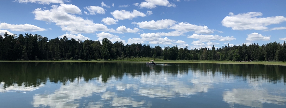 Clouds reflect upon Lake Itasca with evergreen trees behind