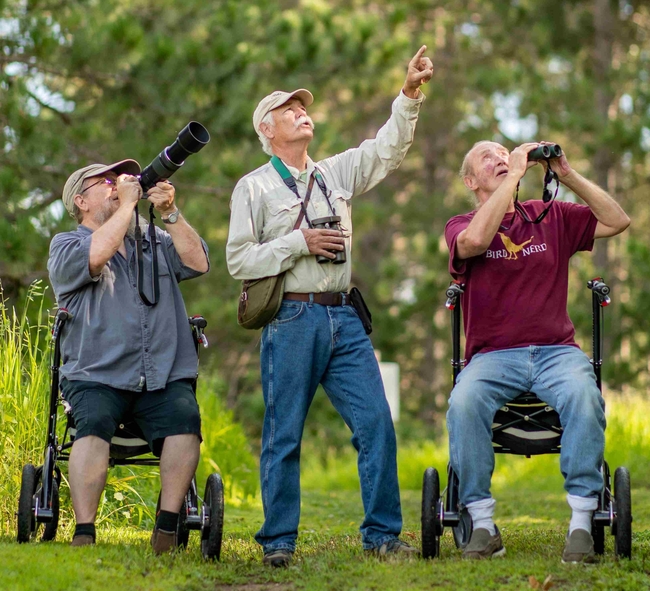 Three men birding, pointing camera, binoculars, or a finger to the sky