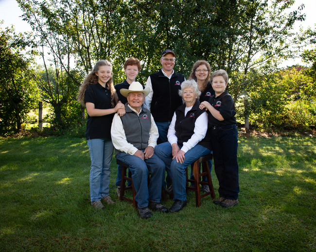 Three generations in one family portrait, with elder couple in front (man wearing cowboy hat), the next generation and their children standing behind