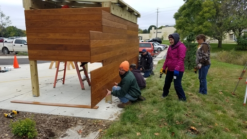 Volunteers with tools are helping to build a wooden bike shed