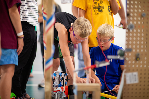 A close up of two boys wearing safety goggles as they work on building a machine.