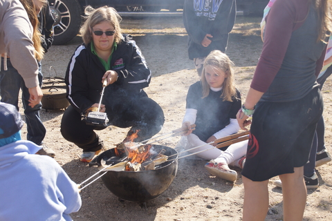 A woman and a group of kids cooking over a campfire.