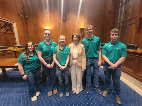 A group of youth members wearing green 4-H polos pose with Senator Amy Klobuchar.