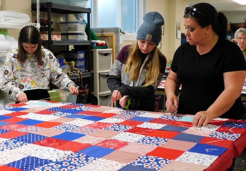 An adult and two teens work on a red, white and blue quilt