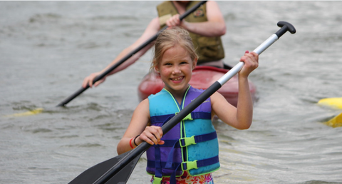 A smiling girl wearing a life jacket paddling in a canoe.
