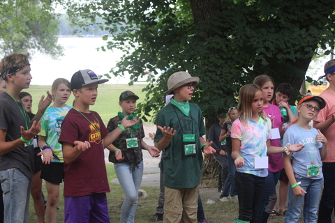 Youth campers standing in a group outside with their hands out as if doing motions to a song.
