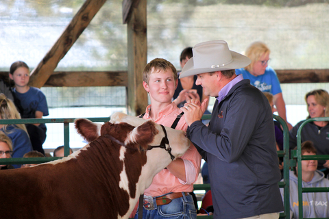 An adult judge is talking with a teenage boy that is exhibiting a beef cattle animal.
