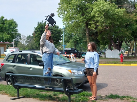 Two teen girls using film equipment outside. 