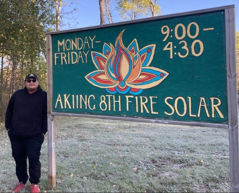 Gwe Gasco standing next to Akiing 8th Fire Solar sign.