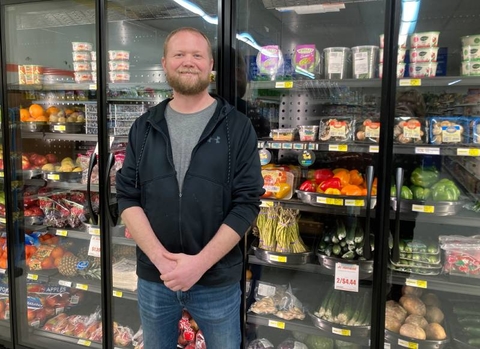 Owner Aaron Bakke stands in front of new coolers displaying fresh produce.