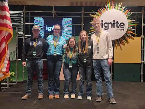 Five youth members in a line in front of a sign reading, "ignite 4-H"