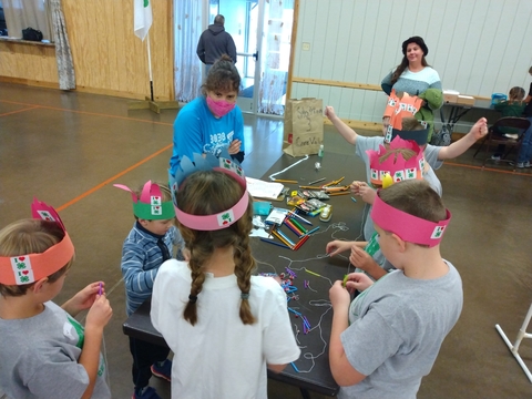 A group of kids wearing paper crowns completing a craft while an adult looks on.