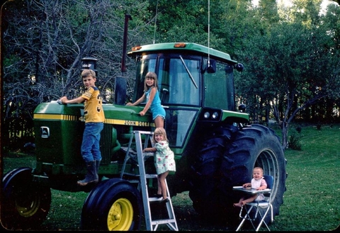 Constance Carlson and her siblings climbing on a John Deere tractor.