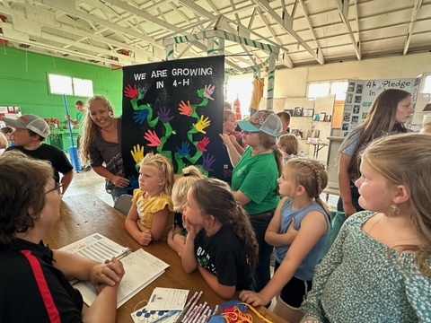 Lindsay Dalluge, 4-H volunteer, and youth members having a club banner judged at a fair.