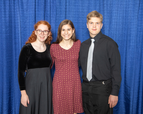three youth stand close, smiling, against a curtain backdrop