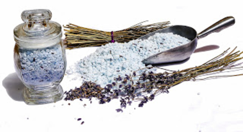 Epsom salts in a jar next to a metal scoop of Epsom salts and dried lavender scattered on a table.