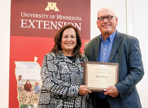 The dean and Kent Thiesse stand together in front of Extension sign while Kent holds award plaque