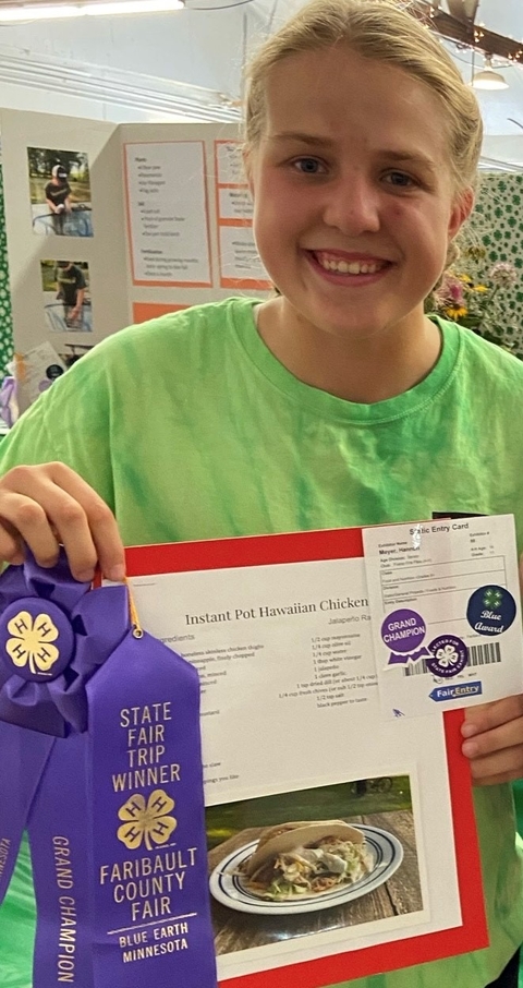Teen girl holds up her the book recipe and her purple ribbons while smiling for the camera.