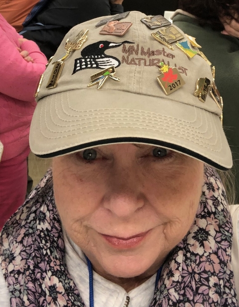 Woman wears a Minnesota Master Naturalist hat with a loon and many pins on it.