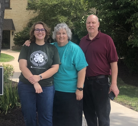 Three people stand smiling for the camera. One is wearing a 4-H Dakota County t-shirt