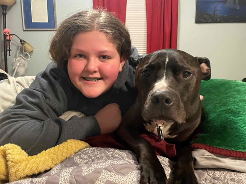 A girl with braces faces the camera with her large black and white dog by her side and a green pillow behind them