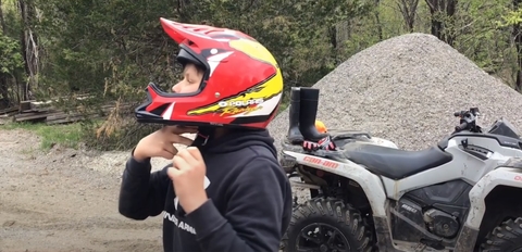 Boy wearing a red helmet standing in front of his ATV as he shows how to adjust strap