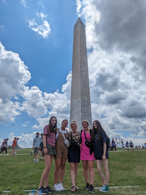 Five girls posing with smiles and linked arms in front of the Washington Monument in Washington, D.C.