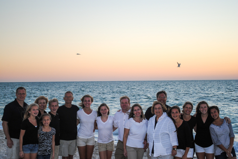 16 family members pose for a family photo with bird flying overhead on beach
