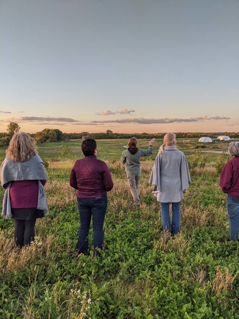 Group socially distanced, standing in a field looking toward a beautiful sunset.